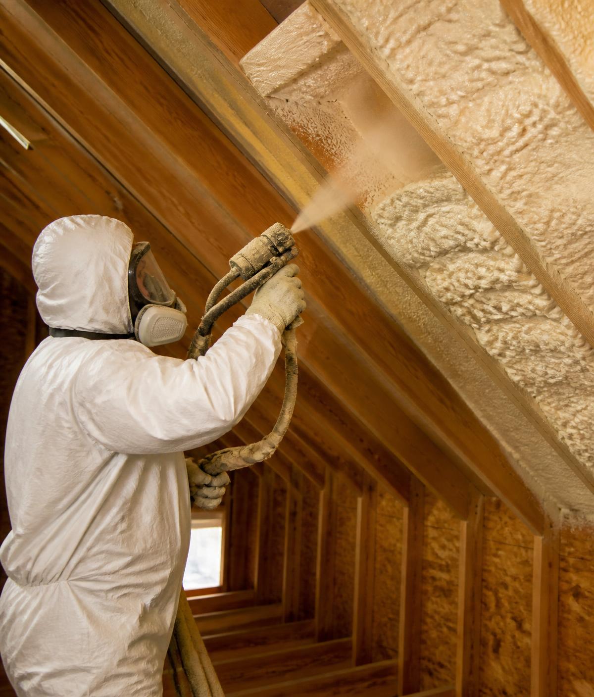 Installer applying spray foam insulation between rafters